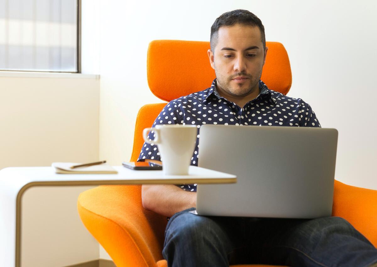 Image of a man sitting on an orange chair and working on a laptop