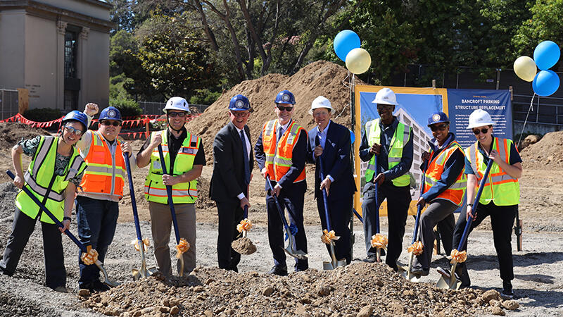 A group of people in hard hats holding shovels break ground on the new parking structure.